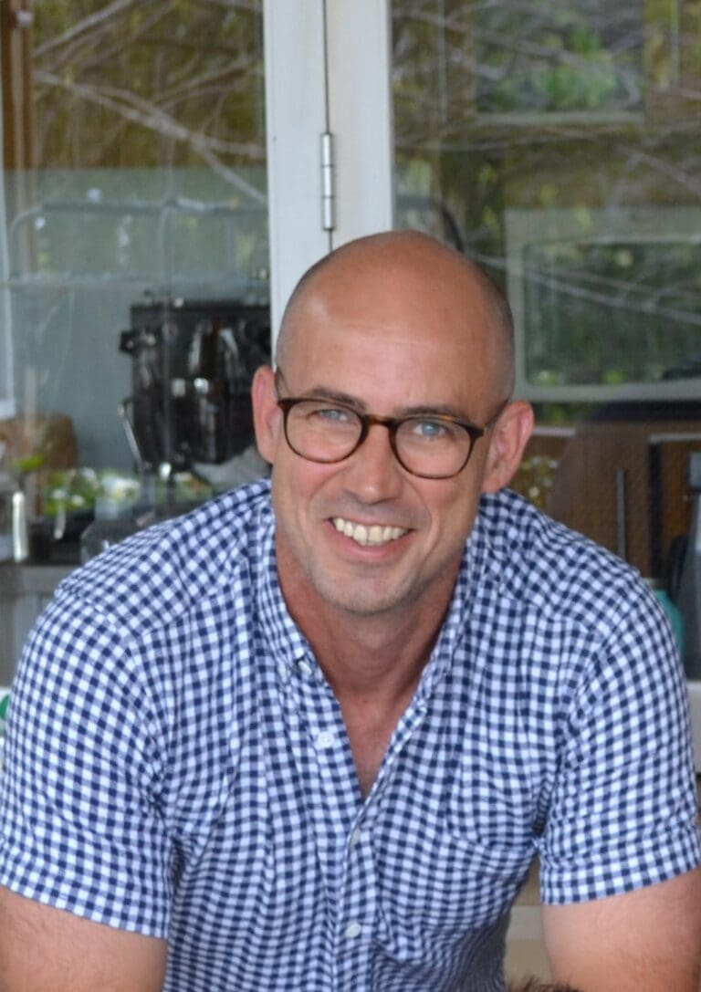 Portrait of a man in a blue shirt smiling with glasses.